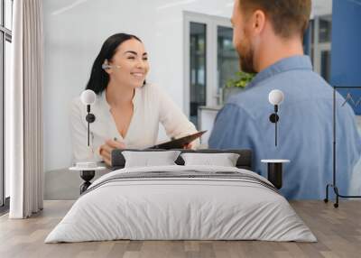 The employee of the beauty salon meets the client in the reception of a modern beauty salon. A man signs a paper with the consent for maintenance. The woman smiles at him Wall mural