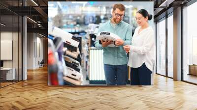 The happy couple chooses wireless vacuum cleaner at store Wall mural