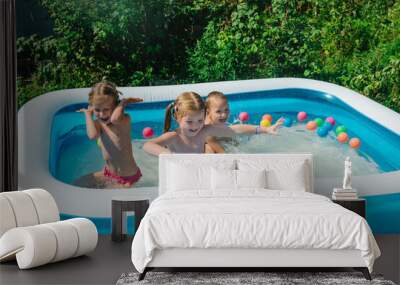 Three happy friends are splashing in an inflatable pool in the garden. Concept of summer season and recreation. Kids having fun together. Children playing and swimming in water on the backyard. Wall mural