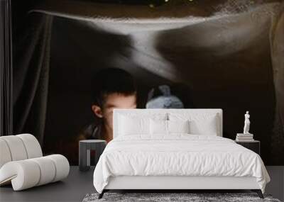 Two children with flashlight read a book under a blanket as a tent Wall mural