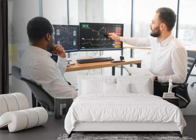 Two diverse colleagues traders talking to each other, sitting in the office in front of multiple computer screens. Stock trading, people, business concept Wall mural