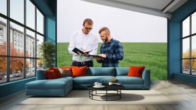 Two farmer standing in a green wheat field and shake hands. Wall mural