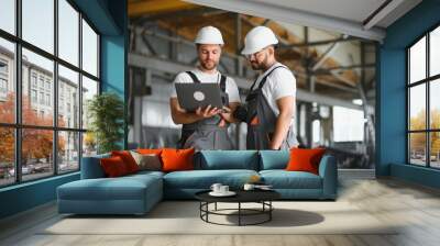 Two Heavy Industry Employees in Hard Hats Discussing Job Assignments at the Factory, Using Laptop Computer Wall mural