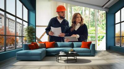 worker in a helmet and customer architect at a construction site inspect plan calculate construction repair. male builder repairman and female boss client in a house under construction use a tablet Wall mural