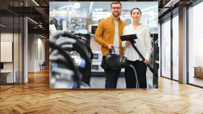 Young beautiful couple buying new vacuum cleaner at tech store. Having fun shopping time Wall mural