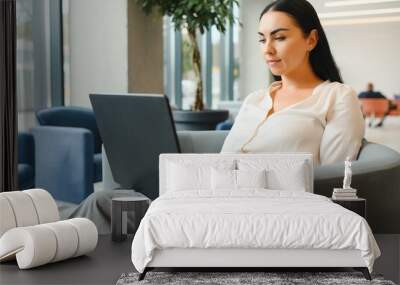 Young business woman sitting at sofa and working with laptop at the waiting hall of the business center Wall mural