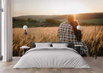 Young couple hugging, standing back, people covered with blanket, at sunset in autumn an outdoor. at field grass on  background of sun. Concept of friendly family. full length. Close Up. Wall mural