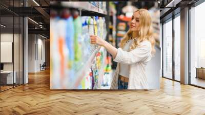 Young glad smiling woman buying household chemicals or laundry detergent at supermarket Wall mural