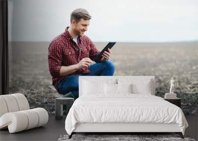 Young handsome farmer squatting in corn field in spring. Agribusiness and innovation concept Wall mural