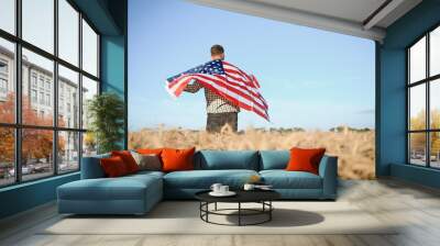 Young patriotic farmer stands among new harvest. Boy walking with the american flag on the wheat field celebrating national independence day. 4th of July concept. Wall mural