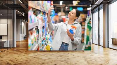 Young woman in household chemistry department of supermarket Wall mural