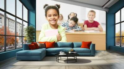 Happy girl keeping books in hands and posing in classroom Wall mural