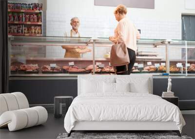 Lady choosing meat behind glass counter. Wall mural