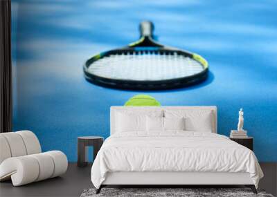 Yellow tennis ball is laying near professional racket on blue cort carpet. Made for playing tennis. Contrast image with satureted colors and shadows. Concept of sport equipment photo. Wall mural