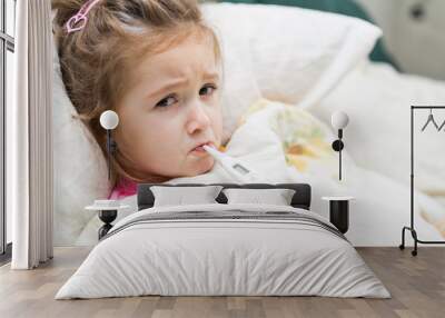 sick little girl holding thermometer laying in bed with grumpy face Wall mural