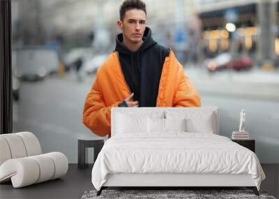 Fashionable man stand on the street near buildings. Wear orange jacket and all black. Winter, autumn outfit. Jacket with blouse and black sneakers. Wall mural