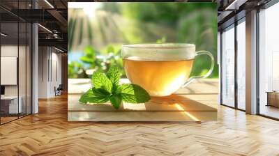 Glass cup of tea with fresh mint leaves on a wooden table, with a blurred garden background and sunlight. Wall mural