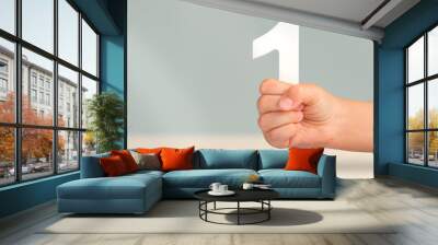 Number one in hand. A hand holds a white number one on a blurred background with copy space. Concept with number one. 1 percent rate, birthday, first or winner. Wall mural