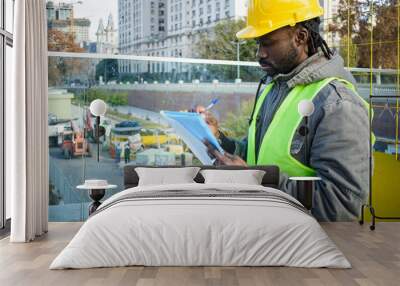 young black engineer man standing supervising the construction site making notes. Wall mural