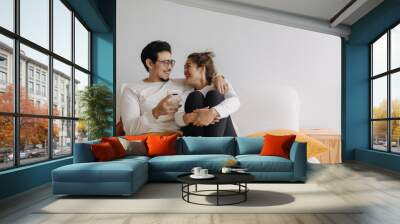 Happy lovely asian couple sharing smartphone to watch together in living room. Wall mural