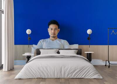 Serious and grumpy Asian man wake up on the bed on blue space background. Wall mural