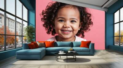 Toddler mixed race girl with small nose and curly brown hair smirking light pink background Wall mural