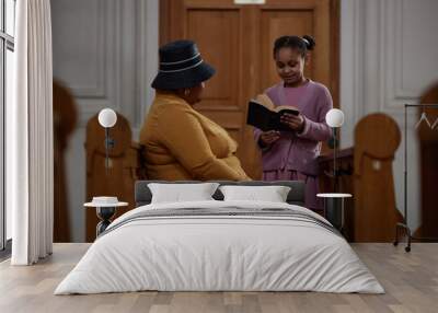 African American little girl reading prayer from Bible to her grandmother during their visit to church Wall mural