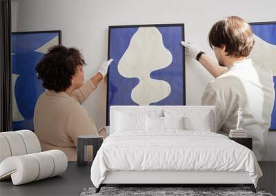 Back view of two people hanging abstract painting on wall while preparing for exhibition in modern art museum Wall mural