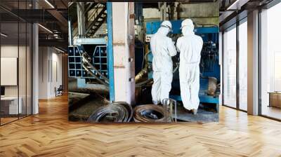 Back view portrait of two factory workers wearing biohazard suits operating machine on modern industrial plant, copy space Wall mural