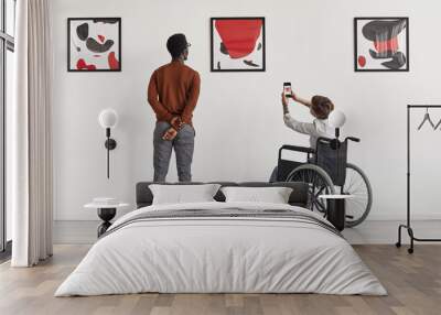 Back view portrait of young woman using wheelchair taking photo of artwork while visiting accessible museum, copy space Wall mural