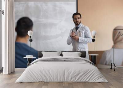 Bearded Muslim man doctor in glasses holding microphone giving speech at medical presentation with dental X-Ray on projection screen in background Wall mural