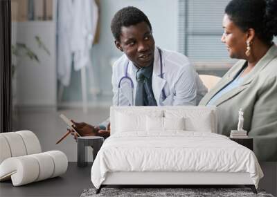 Black young man as doctor consulting female patient in clinic Wall mural