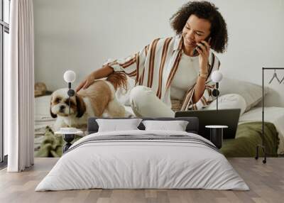 Candid portrait of black young woman working from home on bed and playing with pet dog, copy space Wall mural