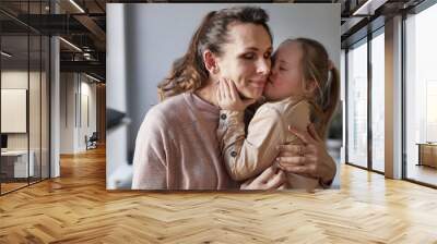 Candid portrait of cute girl with down syndrome kissing and hugging mother lovingly in simple home interior, copy space Wall mural