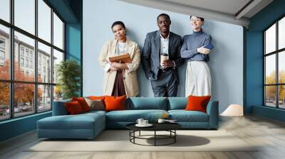 Candid waist up portrait of three diverse business people smiling at camera in office while standing against simple grey background Wall mural