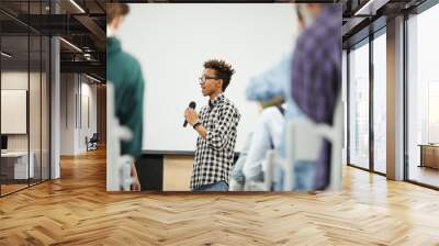 Cheerful confident young black student with Afro hairstyle standing in convention center room and presenting his startup project at conference Wall mural