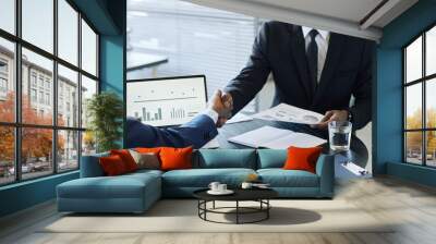 Close up of two impersonal business men shaking hands across meeting table in office after negotiating deal Wall mural