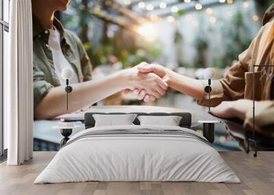 Close-up of unrecognizable business partners sitting at table with papers and laptop and shaking hands after concluding deal in cafe Wall mural