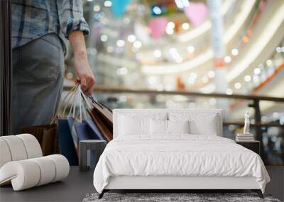 Close-up of unrecognizable woman in casual clothing standing in spacious shopping mall with lights and holding many paper bags Wall mural