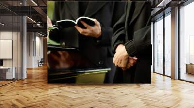 Close up of young woman standing by coffin at outdoor funeral ceremony, priest reading prayer in background, copy space Wall mural