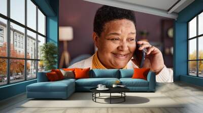 Close up portrait of black senior woman calling by smartphone in home setting and smiling cheerfully talking to loved ones Wall mural