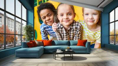 Colorful portrait of three happy kids posing looking at camera while having fun playing in children center Wall mural