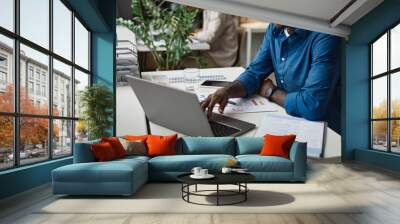 Cropped shot of young African-American man using laptop at desk while working in office Wall mural