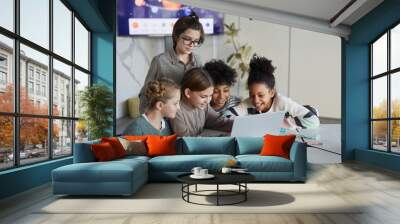 Diverse group of children using laptop together at table in modern school, copy space Wall mural