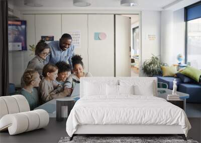 Diverse group of children with male teacher using laptop together in modern school classroom, copy space Wall mural