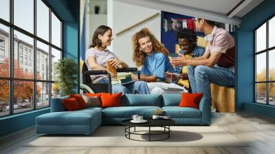 Diverse group of young people chatting in college library including female student with disability Wall mural