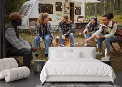 Diverse group of young people roasting marshmallows while enjoying camping with friends in forest, copy space Wall mural