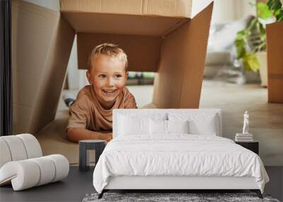 Front view portrait of cute boy playing in cardboard box while family moving to new house, copy space Wall mural