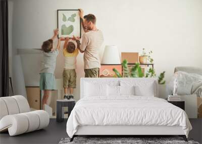 Full length portrait of happy father with two sons hanging pictures on wall while moving in to new home, copy space Wall mural