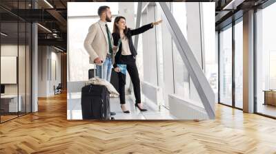 Full length portrait of modern couple holding airplane tickets and suitcases walking to gate in modern airport Wall mural